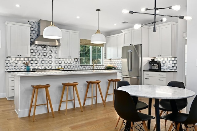kitchen featuring high end fridge, a kitchen breakfast bar, a center island, wall chimney exhaust hood, and backsplash