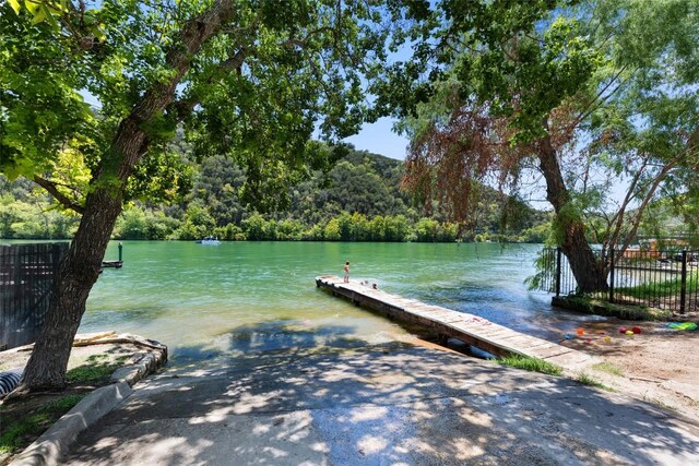 view of dock with a water view, a view of trees, and fence