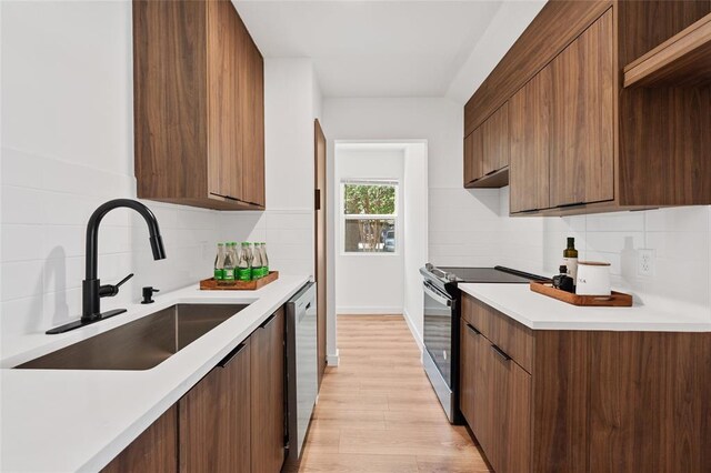 kitchen with electric range, a sink, backsplash, stainless steel dishwasher, and modern cabinets