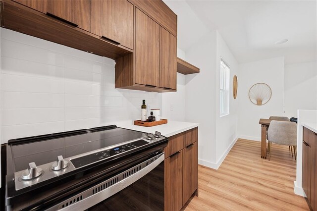 kitchen featuring stainless steel electric stove, baseboards, brown cabinets, and light countertops