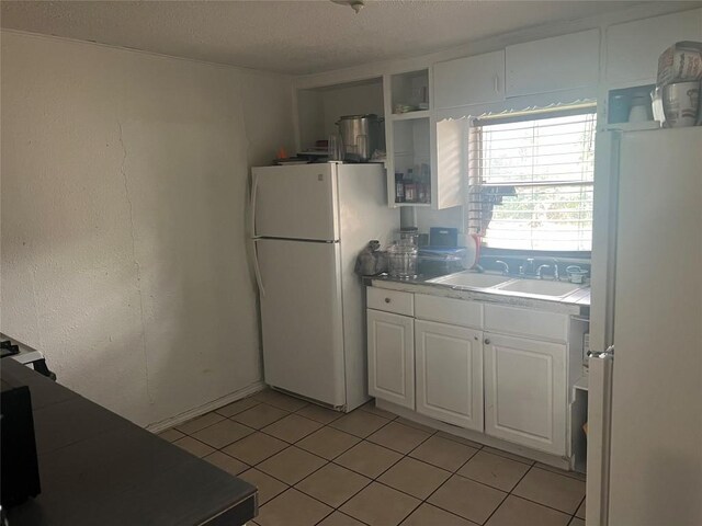 kitchen featuring freestanding refrigerator, white cabinetry, light tile patterned flooring, and a sink