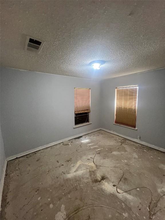 spare room featuring baseboards, a textured ceiling, and visible vents