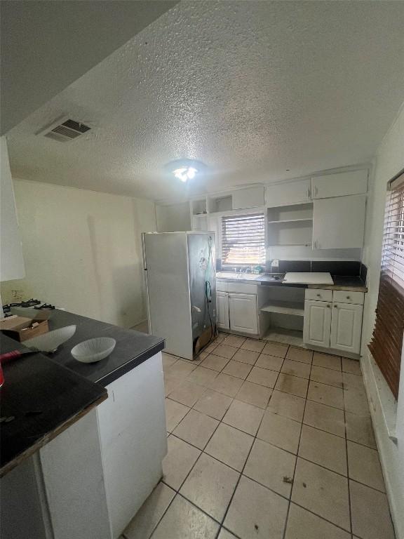 kitchen with freestanding refrigerator, light tile patterned flooring, open shelves, and dark countertops