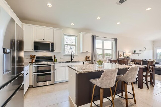 kitchen with appliances with stainless steel finishes, a healthy amount of sunlight, light tile patterned floors, and tasteful backsplash