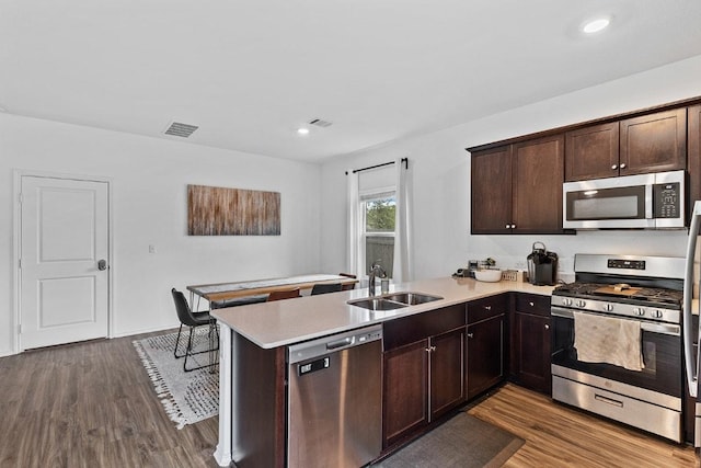 kitchen with visible vents, a peninsula, dark wood-type flooring, a sink, and stainless steel appliances