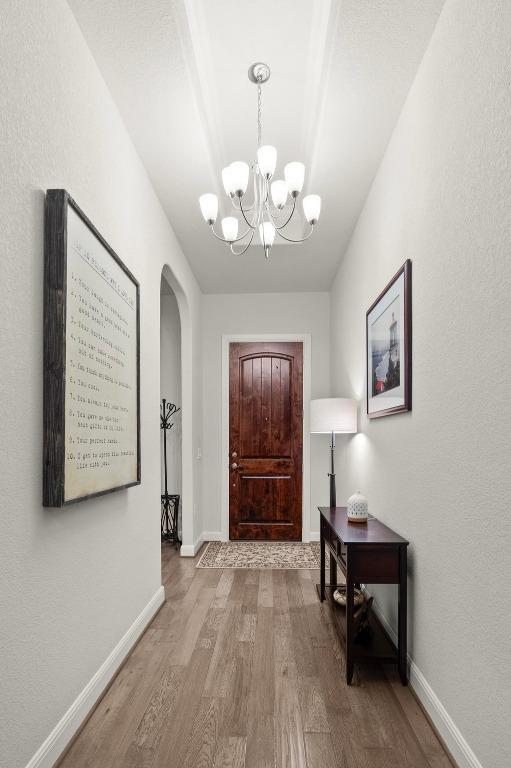 foyer featuring baseboards, arched walkways, wood finished floors, and a notable chandelier