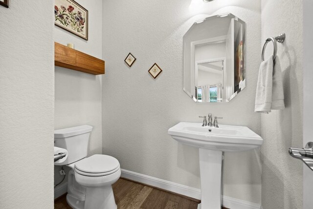 half bath featuring toilet, baseboards, a sink, and wood finished floors