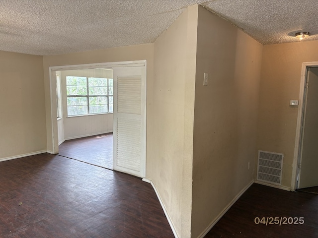 hallway featuring baseboards, a textured ceiling, visible vents, and wood finished floors