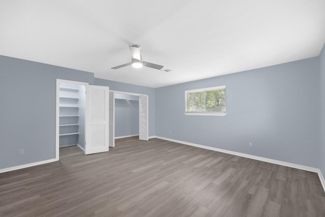 unfurnished bedroom with wood finished floors, baseboards, two closets, and a ceiling fan