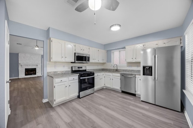4411 Cumbria Ln, Austin, TX 78727 - kitchen with appliances with stainless steel finishes, a ceiling fan, light wood finished floors, white cabinetry, and a stone fireplace