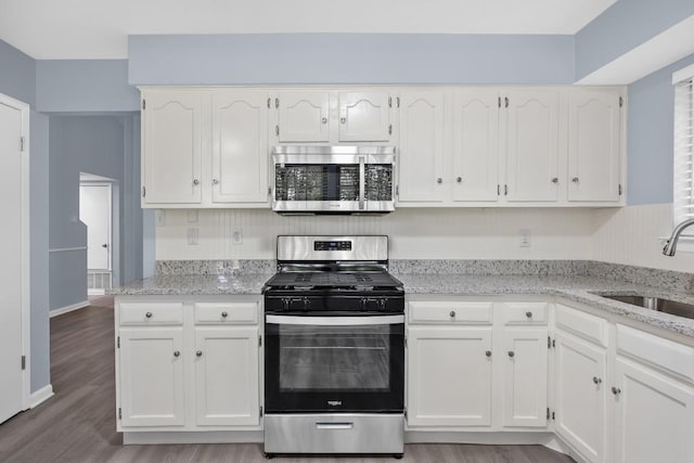 kitchen featuring appliances with stainless steel finishes, a sink, white cabinetry, light stone countertops, and light wood finished floors