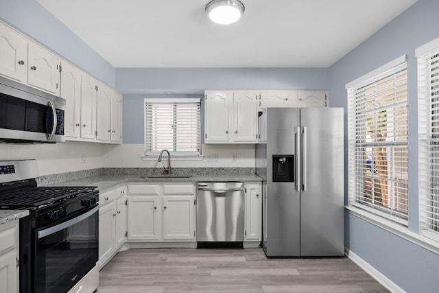 kitchen featuring appliances with stainless steel finishes, a sink, white cabinetry, and plenty of natural light