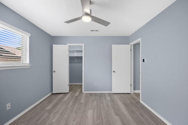 unfurnished bedroom featuring wood finished floors, baseboards, a walk in closet, a closet, and ceiling fan