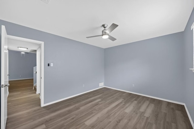 unfurnished room with dark wood-style flooring, a ceiling fan, and baseboards
