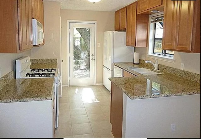 kitchen featuring white appliances, light stone counters, brown cabinetry, and a sink