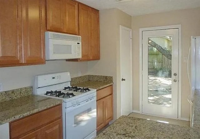 kitchen with brown cabinetry, white appliances, and light stone countertops