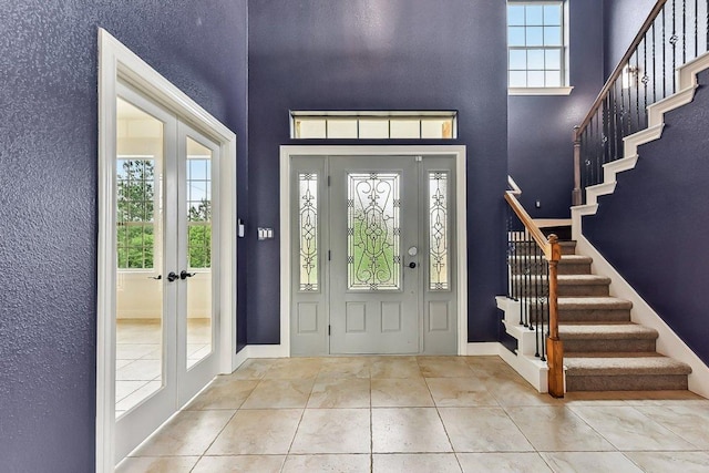 foyer featuring a towering ceiling, baseboards, stairway, tile patterned floors, and french doors