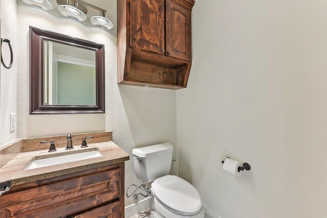 half bathroom with toilet, baseboards, and vanity
