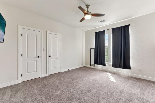 unfurnished bedroom featuring baseboards, carpet flooring, a ceiling fan, and visible vents