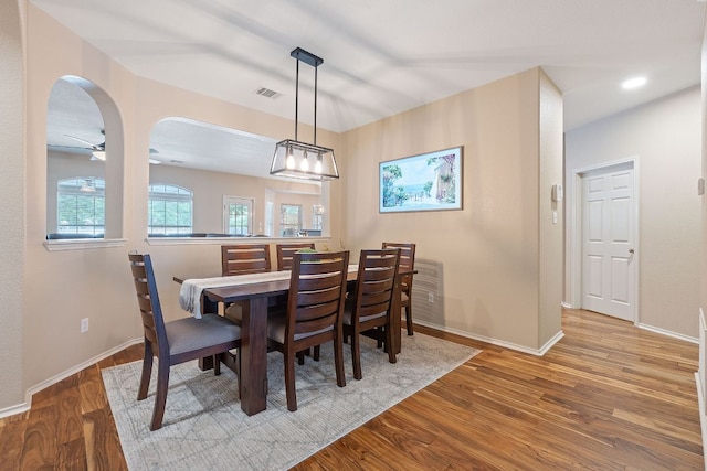 dining area with arched walkways, baseboards, visible vents, and wood finished floors