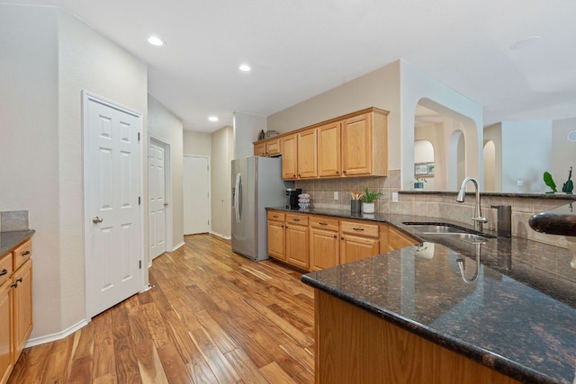 kitchen with stainless steel fridge, a sink, dark stone counters, decorative backsplash, and light wood-type flooring