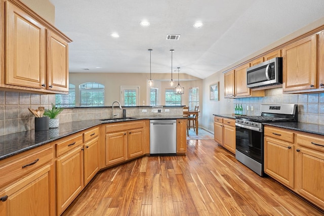 kitchen with visible vents, a peninsula, a sink, light wood finished floors, and appliances with stainless steel finishes
