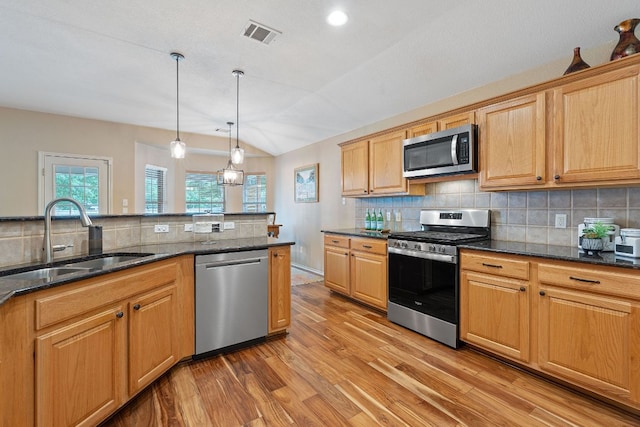 kitchen with appliances with stainless steel finishes, a sink, light wood-style flooring, decorative backsplash, and visible vents