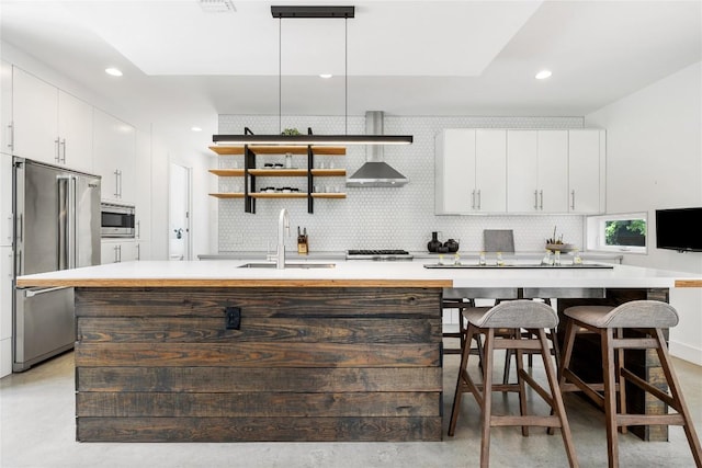 kitchen featuring appliances with stainless steel finishes, a sink, light countertops, a kitchen island with sink, and backsplash