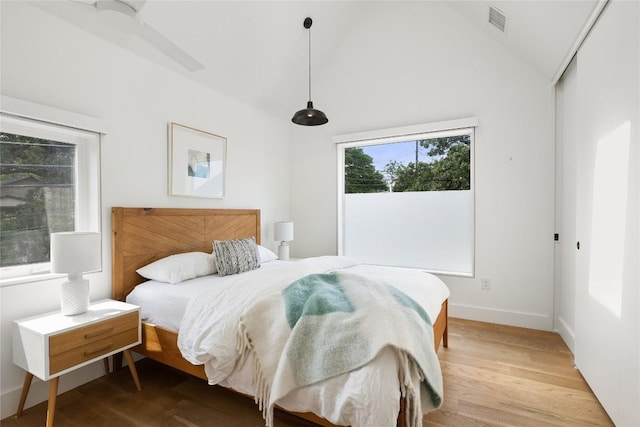 bedroom with visible vents, baseboards, light wood finished floors, and lofted ceiling