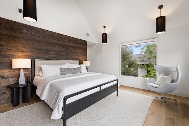 bedroom featuring high vaulted ceiling, baseboards, wood finished floors, and visible vents