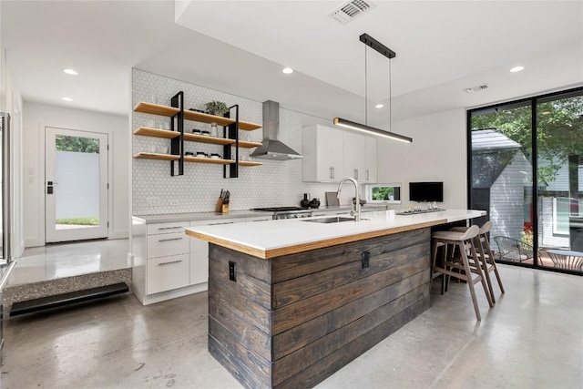 kitchen with visible vents, modern cabinets, wall chimney exhaust hood, tasteful backsplash, and a sink