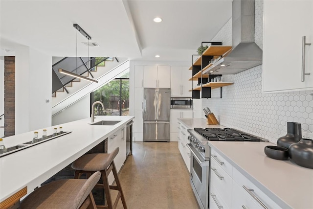 kitchen featuring decorative backsplash, wall chimney range hood, high quality appliances, white cabinets, and a sink