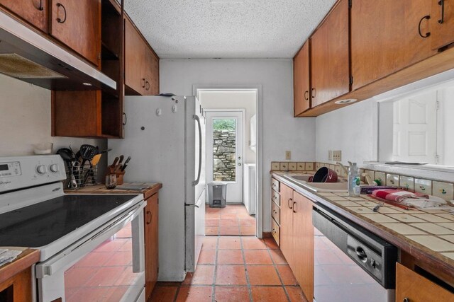 kitchen featuring white range with electric cooktop, brown cabinets, dishwasher, tile counters, and under cabinet range hood