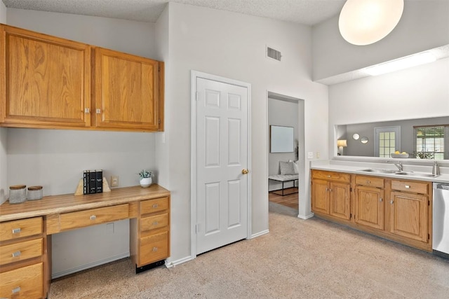 kitchen featuring visible vents, light colored carpet, light countertops, built in desk, and a sink