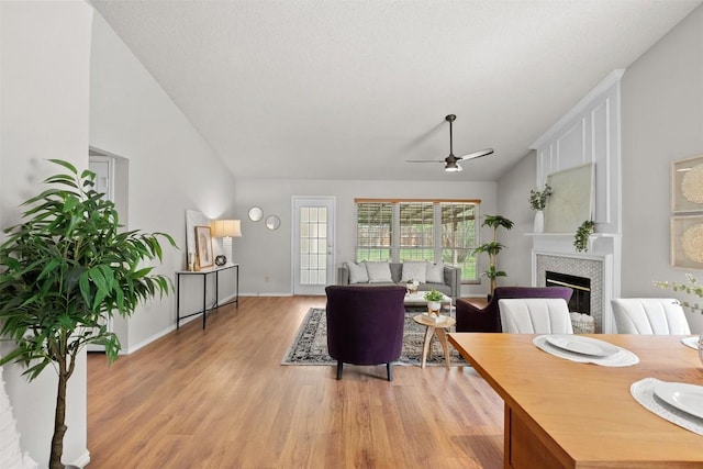 living room with a fireplace, baseboards, a ceiling fan, light wood finished floors, and vaulted ceiling