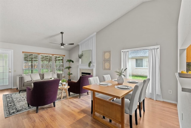 dining area featuring a ceiling fan, light wood finished floors, a wealth of natural light, and a tile fireplace