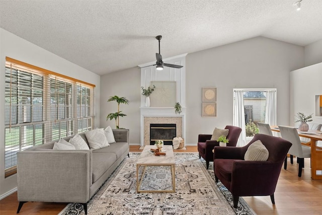 living room with wood finished floors, a fireplace, ceiling fan, a textured ceiling, and vaulted ceiling