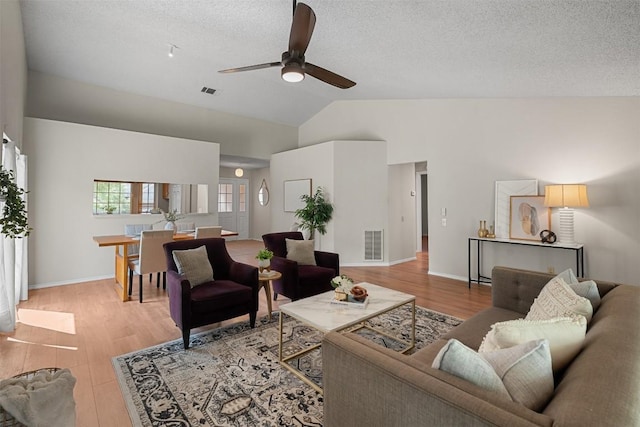 living area with visible vents, lofted ceiling, ceiling fan, light wood-type flooring, and a textured ceiling