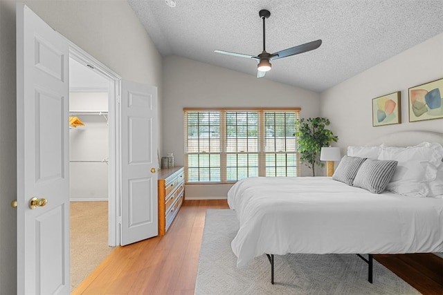 bedroom with a textured ceiling, a ceiling fan, lofted ceiling, light wood-type flooring, and a spacious closet