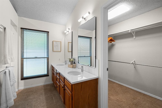 bathroom with baseboards, a sink, a textured ceiling, and a spacious closet