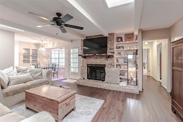 living area featuring a ceiling fan, a fireplace, wood finished floors, and beam ceiling