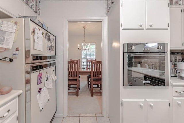 kitchen with an inviting chandelier, freestanding refrigerator, oven, light countertops, and white cabinetry