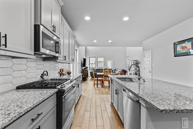 kitchen featuring decorative backsplash, a sink, light wood finished floors, gray cabinetry, and stainless steel appliances