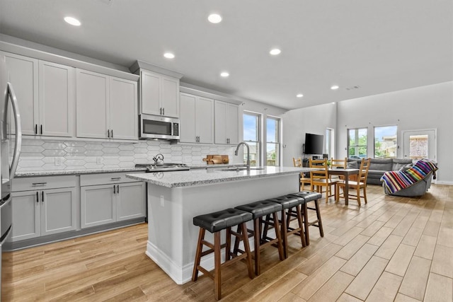 120 Freeman Loop, Liberty Hill, TX 78642 - kitchen featuring stainless steel microwave, open floor plan, light wood-type flooring, tasteful backsplash, and recessed lighting