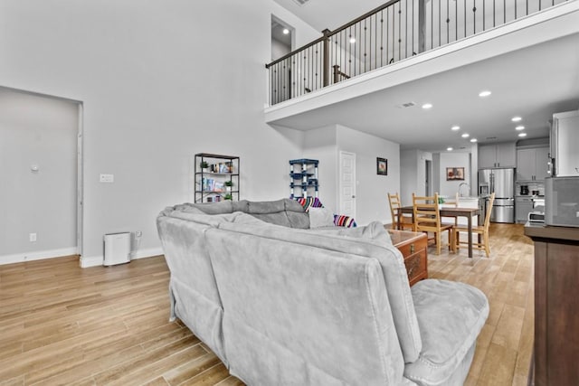 living room with light wood-type flooring, recessed lighting, baseboards, and a high ceiling