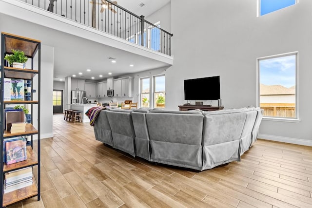 living room with a high ceiling, a healthy amount of sunlight, and light wood-style flooring