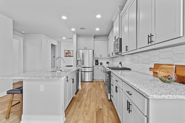 120 Freeman Loop, Liberty Hill, TX 78642 - kitchen with stainless steel appliances, light wood finished floors, a kitchen breakfast bar, an island with sink, and tasteful backsplash