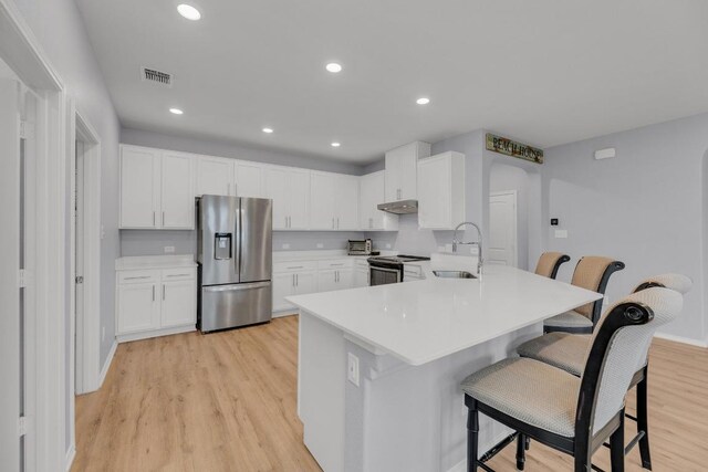 kitchen with appliances with stainless steel finishes, a sink, a kitchen breakfast bar, under cabinet range hood, and visible vents