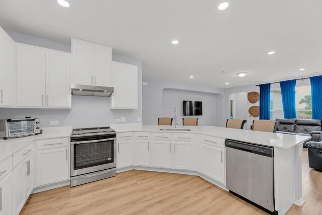 kitchen featuring a toaster, open floor plan, light countertops, under cabinet range hood, and appliances with stainless steel finishes