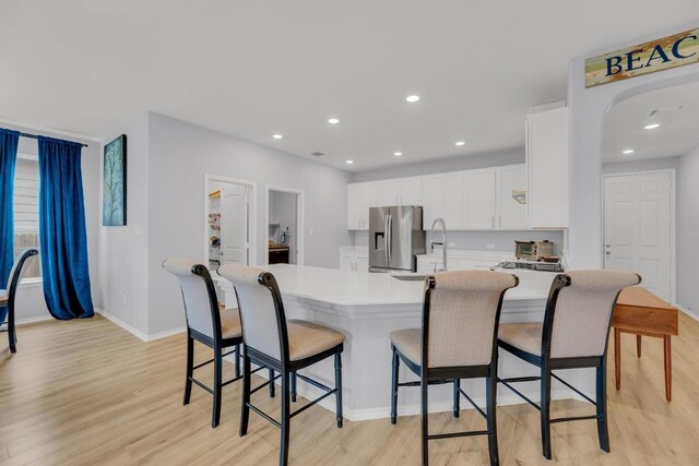 kitchen featuring a kitchen bar, light wood-type flooring, light countertops, stainless steel fridge, and white cabinetry